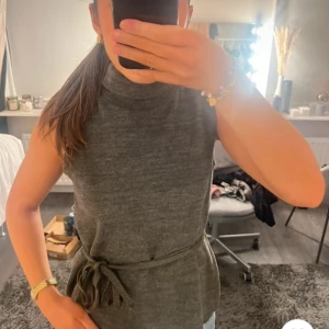 Mörk grön ärmlös topp med knytband - Snygg mörk grön ärmlös topp med hög krage och knytband i midjan. Perfekt för dig som gillar en enkel men stilren look. Materialet känns mjukt och har en lätt stickad känsla. Nästan aldrig använd.