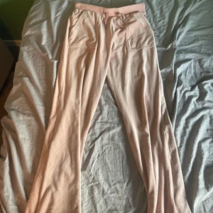 Rosa mjukisbyxor från Juicy Couture - Supermysiga ljusrosa mjukisbyxor från Juicy Couture med snörning i midjan och bakficka med tryckknappar. Byxorna är i mjuk velour och har en relaxed passform, perfekta för chill dagar. Klassisk Juicy-detalj på snöret och logga på fickan.