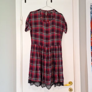 Rutig röd klänning från FB Sister - Supersöt kort rutig klänning från FB Sister. Klänningen har korta ärmar, rund halsringning och svart spetsdetalj längst ner.