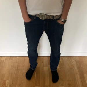 Mörkblå jeans med slim fit - Säljer ett par mörkblå jeans med snygg slim passform och klassiska kontrastsömmar. Jeansen har fem fickor och normal midja. Perfekta till sneakers och t-shirt för en clean look.Obs har en liten vit fläck på en av fickorna. Modellen är 180 ungefär