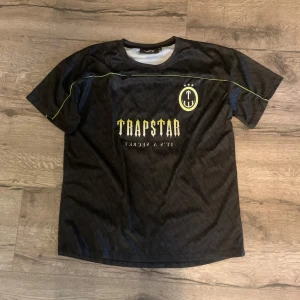 Svart Trapstar t-shirt med tryck - Svart t-shirt från Trapstar med gul text och tryck både fram och bak. Stora siffran 22 på ryggen och coola detaljer med neongula linjer över bröst och ärmar. Tillverkad i luftig polyester, perfekt för en streetwear-look.