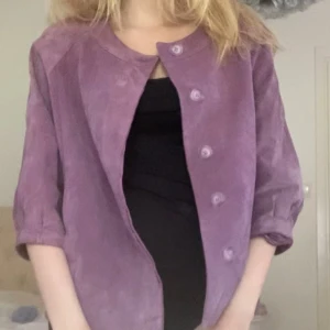 Lila trekvartsärm manchesterjacka med knappar - Säljer en lila manchesterjacka med rund halsringning och knäppning framtill. Jackan har trekvartsärmar och en loose passform, perfekt för dig som gillar en chill och trendig look. Färgen är riktigt snygg och materialet känns mjukt. Storlek L men passar XS-m beroende på hur man vill ha den