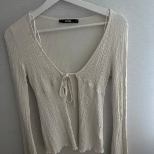 Vit långärmad topp från Bik Bok - Säljer en vit långärmad topp från Bik Bok med knytning framtill och lätt rynkad struktur. Toppen har v-ringning och är tillverkad i ett mjukt, syntetiskt material. Perfekt för att skapa en stilren och trendig look. Storlek är Xs, men väldigt stretchig passar även om du har storlek S. 
