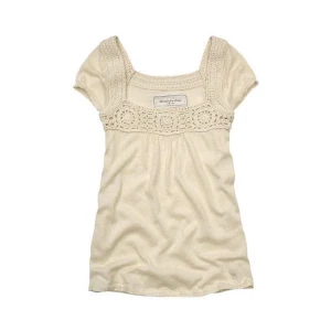 Beige Abercrombie & Fitch topp med virkad detalj - Supersöt topp  från Abercrombie & Fitch med korta ärmar och fyrkantig ringning. Ovanför bysten finns en bred virkad kant med blommönster som ger en bohemisk vibe. Perfekt till jeans eller kjol för en chill look.
