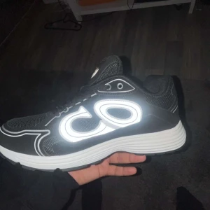 Svarta sneakers med reflekterande detaljer - Svarta sneakers med vit, tjock sula och stora reflekterande CD-detaljer på sidorna. Ovandelen är i mesh och syntet, med snörning och sportig vibe. Perfekta för dig som vill sticka ut med coola detaljer och bekväm passform.