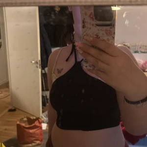 Svart ribbad croppad linnetopp från SHEIN - Säljer en svart ribbad croppad linnetopp från SHEIN med smala axelband och asymmetrisk halsringning. Toppen är stretchig och sitter tight, perfekt till sommaren. Enkel och stilren design.