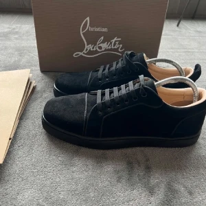 Svarta sneakers från Christian Louboutin i mocka - Säljer ett par svarta sneakers från Christian Louboutin i mjuk mocka med klassisk röd sula. Skorna har snörning och rund tå, samt diskret broderad logga på hälen. Perfekta för dig som gillar stilrena och exklusiva sneakers.