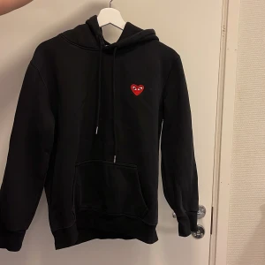 Svart hoodie från Comme des Garçons Play - Svart hoodie med huva och dragsko från Comme des Garçons Play. Klassisk design med hjärtloggan på bröstet och stor magficka framtill. Står storlek M men är mer som en S.