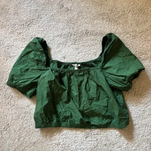 Grön croppad topp med puffiga ärmar - Säljer en grön croppad topp med puffiga korta ärmar och resår i nederkant och halsringning. Toppen har en luftig passform och är tillverkad i bomull, perfekt för varma dagar.