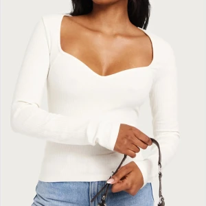 Vit ribbad långärmad topp med sweetheart-urringning - Säljer en vit långärmad topp med ribbad struktur och snygg sweetheart-urringning. Toppen har figurnära passform och är perfekt att styla med jeans eller kjol. Enkel men trendig design.