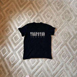 Svart t-shirt från Trapstar London - Säljer en svart t-shirt från Trapstar London med stor vit logga på bröstet. Klassisk passform och rund halsringning. Perfekt för dig som gillar streetwear och vill ha något stilrent men ändå med attityd. Aktiv 24/7✅ Skickas inom 24h📦🚚 Kan gå ner i hugget 😃✅ Hör av er via frågor⁉️