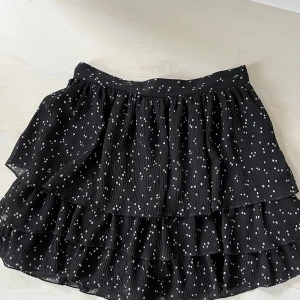 Svart volangkjol med prickar från Zara - Supersöt svart kortkjol från Zara med vita prickar och flera lager volanger. Kjolen har shorts inuti! 