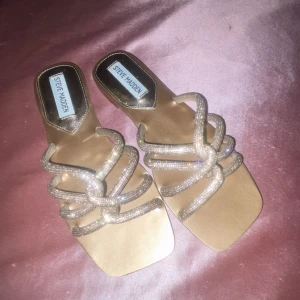 Glittriga sandaler från Steve Madden - Säljer ett par snygga sandaler från Steve Madden i beige med glittriga remmar. Skorna har fyrkantig tå och flera tunna remmar täckta av små strass-stenar som ger en riktigt lyxig vibe. Perfekta för att lyfta vilken outfit som helst. Aldrig använda