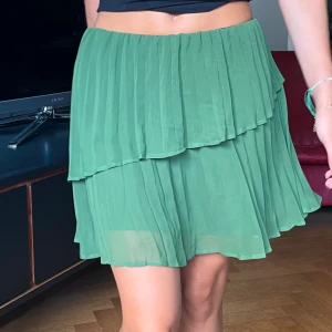 Grön plisserad kortkjol med volang - Grön Zara kjol, knappt använd. Super fina volangdetaljer, brukar även vika ner kanten så den blir lite kortare;) Eller ha den som topp!  Storlek xs 