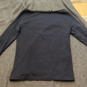 Svart långärmad topp från 157 - En stilren svart långärmad topp från 157 i mjuk bomullsblandning med lite stretch. Enkel och clean design med rund halsringning, perfekt att matcha med jeans eller kjol. Materialet är 94% bomull och 6% elastan för en bekväm passform.