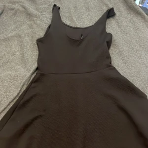 Svart ärmlös klänning - En stilren svart klänning med ärmlös design och rundad halsringning. Klänningen har en lätt utställd kjol och enkel, klassisk siluett som passar perfekt till många olika tillfällen.