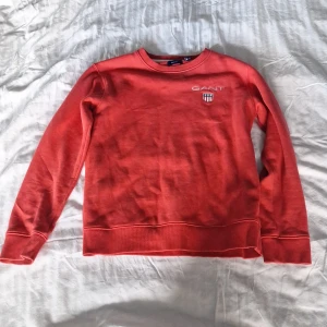 Röd sweatshirt från GANT - Säljer en röd sweatshirt från GANT med broderad logga och sköld på bröstet. Tröjan har rund halsringning, långa ärmar och ribbade muddar. Perfekt för dig som gillar klassisk och stilren streetwear.