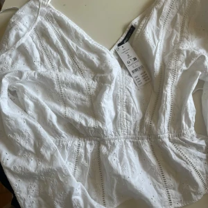 Vit broderad blus från Gina Tricot - Superfin vit blus från Gina Tricot med broderade detaljer och små hålmönster. Blusen har v-ringning, lång ärm och elastisk midja som ger en snygg passform. Perfekt för vår och sommar när du vill ha en luftig och söt topp!!💕💕