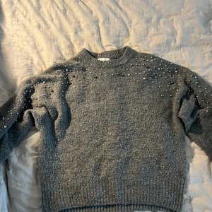 Grå stickad tröja med pärlor -  Grå stickad tröja med pärldetaljer över axlar och bröst.