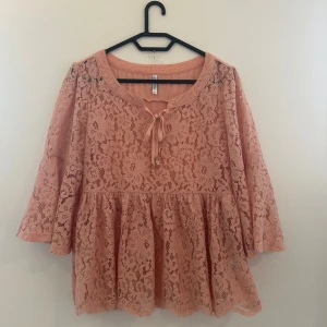 Rosa spetsblus från Chiara Forthi - Supersöt ljusrosa blus i spets från Chiara Forthi. Blusen har blommigt mönster, trekvartsärmar med lätt utsvängd form och knytning vid halsen. Den har en volangkant nedtill och är fodrad under spetsen.