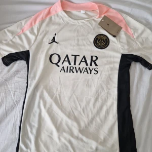 PSG x Jordan fotbollströja och shorts S - Säljer ett PSG x Jordan matchställ i storlek S. Tröjan är vit med svarta och ljusrosa detaljer, PSG-emblem och Jordan-logga på bröstet samt Qatar Airways-tryck. Shortsen är svarta med rosa inslag och PSG-märke. Tillverkad i lätt och ventilerande polyester.