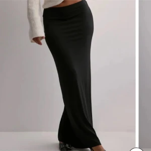 Svart långkjol  - Snygg svart långkjol med figurnära passform och mjukt, stretchigt material. Kjolen har en enkel och stilren design som sitter högt i midjan och faller snyggt längs kroppen. Perfekt att styla med en croppad tröja eller boots.