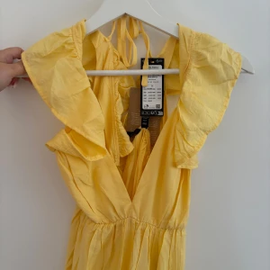 Gul långklänning från Vero Moda - Superfin gul långklänning från Vero Moda med volangdetaljer vid axlarna och v-ringad hals. Klänningen har knytband i nacken och är tillverkad i ett lätt och luftigt material, perfekt för varma dagar.!!😍💛💛 något genomskinlig nertill! 