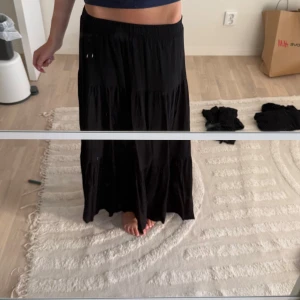 Svart långkjol från Stradivarius - Svart långkjol från Stradivarius i storlek S. Kjolen har en flowy och luftig passform med flera volanger och resår i midjan. Perfekt för dig som gillar en enkel men snygg stil. Materialet känns mjukt och bekvämt.