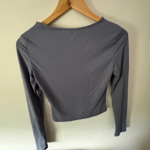 Grå långärmad croppad topp - En stilren grå långärmad topp med croppad passform. Toppen har en enkel, rund halsringning och är tillverkad i ett mjukt och stretchigt material som sitter snyggt på kroppen. Perfekt att matcha med höga jeans eller kjol för en clean look.