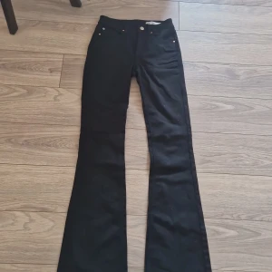 Svarta bootcut jeans från Vero Moda - Svarta jeans från Vero Moda med bootcut-modell och klassisk femficksdesign. Byxorna har lite högre midja och snygga kopparfärgade nitar. Materialet är stretchigt denim som sitter skönt och formar sig efter kroppen.