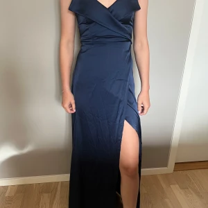 Mörkblå långklänning från Shein Belle - Perfekt till balen, bröllop eller annan högtid!  Supersnygg mörkblå långklänning från Shein Belle med smala axelband, omlott-detalj vid bysten och en hög slits på ena sidan. Klänningen har en elegant satinliknande yta och figurnära passform som ger en lyxig känsla.