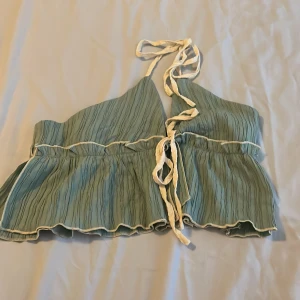 Grön omlott linnetopp med knyt - Supersöt ljusgrön omlott linnetopp med vita knytband i halsen. Toppen har volangkant nedtill och struktur i tyget som ger en cool effekt. Perfekt för varma dagar och ger en chill vibe till din outfit.Nyskick…