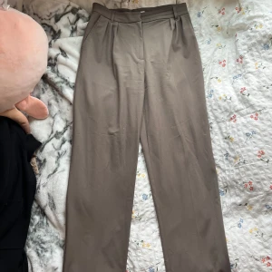 Beige kostymbyxor med raka ben - Snygga beige kostymbyxor med klassisk passform och raka ben. Byxorna har pressveck, hällor för bälte och sidofickor fram samt en bakficka med knapp. Perfekta för en clean och stilren look.