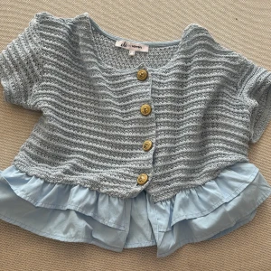 Ljusblå stickad blus från Olé by Koton - Supersöt ljusblå stickad blus med kort ärm och guldiga knappar framtill. Storleken är L men är mycket mindre passar en 12-13 åring