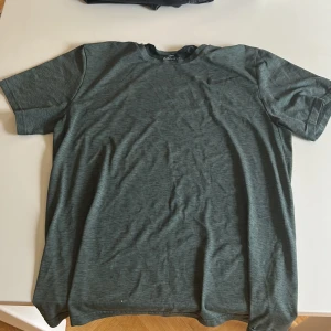 Nike Dri-Fit grön t-shirt herr L - Nike Dri-Fit t-shirt i snygg grön med diskret melerat mönster. Klassisk rund hals och korta ärmar. Perfekt för träning med lätt och snabbtorkande material. Nike loggade bröstet.