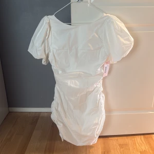 Vit kort klänning med puffärmar och öppen rygg  - Supersfin vit kort klänning från Nelly med puffiga korta ärmar och snygg rynkdetalj längs sidorna och ryggen. 