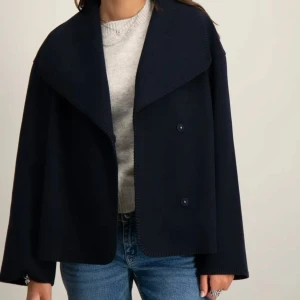 Mörkblå jacka - Snygg mörkblå jacka med bred krage och dubbelknäppning framtill. Jackan har en rak och loose passform, långa ärmar och är tillverkad i ett mjukt ullmaterial. Perfekt för dig som gillar stilren och enkel design.