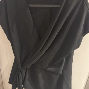 Svart omlottopp med knyt - Snygg svart omlottopp med korta ärmar och knyt i sidan. 