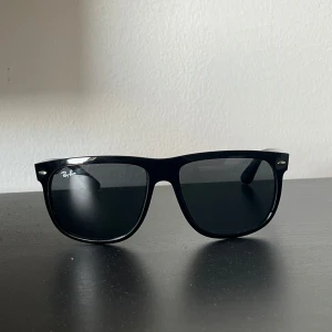 Svarta Ray-Ban solglasögon - Klassiska svarta Ray-Ban solglasögon med glansig finish och mörka glas. Snygg och tidlös design med breda skalmar och diskret logga på sidan. Perfekta för att lyfta din stil under soliga dagar. ”Pris kan diskuteras”