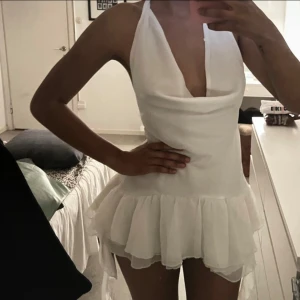 Vit volangklänning  - Supersöt vit kortklänning från Missguided med volangkant och djup v-ringning. Klänningen är ärmlös med halterneck och öppen rygg, passar Xs-M