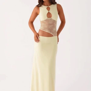 Lång ljus klänning med spets och cut-outs - Supersnygg lång klänning i ljusgul ton med transparent spetsdetalj över midjan och coola cut-outs framtill och baktill. Ärmlös modell med rund hals och öppen rygg. Perfekt för dig som vill sticka ut med en unik och trendig look.