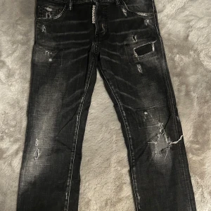 Svarta Dsquared2 jeans med slitningar - Snygga svarta jeans från Dsquared2 med coola slitningar och distressed detaljer. Jeansen har rak passform, klassiska fem fickor och Dsquared2-logga vid gylfen. Tillverkade i bomull med en skön känsla och trendig look.