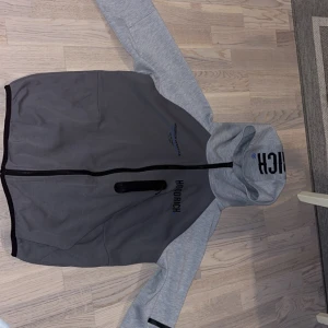 Grå hoodie med dragkedja från Hoodrich med luva - Snygg tvåfärgad hoodie från Hoodrich med grå kropp och ljusgrå ärmar och huva. Hoodien har dragkedja hela vägen, tryck på bröstet och ryggen samt en praktisk ficka med dragkedja. Perfekt för dig som gillar streetwear och vill sticka ut. Den passar främst Storlek S men även M väldigt bra det är en favorit men passar tyvärr inte längre mig