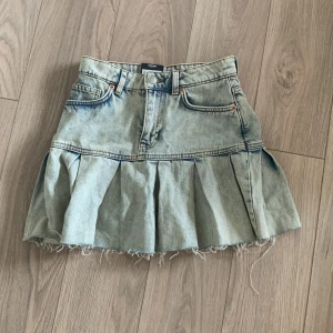 Plisserad jeanskjol från Monki - Säljer en ljusblå plisserad jeanskjol från Monki med rå kant nertill och klassiska fickor fram och bak. Kjolen är en kort modell. Perfekt för dig som gillar denim och vill ha en kjol med lite edge!Säljer pga förliten.