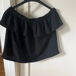 Svart offshoulder topp med volang - Snygg svart offshoulder topp med bred volang runt hela överdelen. Blusen är i storlek M men skulle mer säga att den passar en S