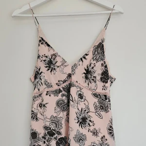 Sommarklänning med blommigt mönster  - Ljusrosa sommarklänning i storlek S med svart blommönster & smala axelband. V-ringad framtill med litet spänne i ryggen. Använt få gånger - inga fläckar eller skador                