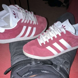 Adidas Gazelle rosa mockasneakers - HELST I GÖTEBORG ELLER I NÄRHETEN DÅ JAG KAN MÖTAS UPP Säljer ett par Adidas Gazelle sneakers i snyggt rosa mocka med klassiska vita ränder och vit sula. Skorna har rund tå, platt sula och vita snören. Perfekta för dig som vill ha en ikonisk och stilren sneaker med retrovibbar. 2 månader gamla då jag redan tröttnat på de