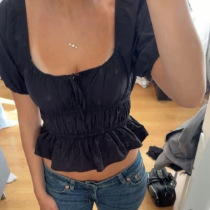 Svart croppad blus med puffärm - Supersöt svart blus med croppad passform, puffiga korta ärmar och volang nertill. Gullig och aldrig använd. Tveka inte på att fråga om du undrar något! 💌