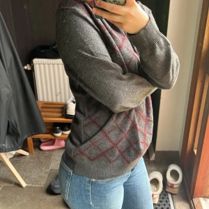Grå rutig stickad polotröja - Mysig grå stickad tröja med vinröda rutmönster över hela framsidan. Tröjan har polo ringning, ribbade muddar och lång ärm. Inga defekter. ❣️