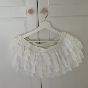 Vit volangkjol från Monki - Superfin vit kortkjol från Monki med flera lager volanger som ger en fluffig och lekfull look. Kjolen har resår i midjan för skön passform och är gjord i ett lätt, flowy material. Perfekt för dig som vill sticka ut lite extra!